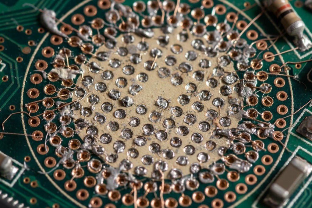 A macro photo showing the footprint of a removed BGA chip on a circuit board, where several small copper pads have been torn away, revealing the lighter fiberglass material underneath.