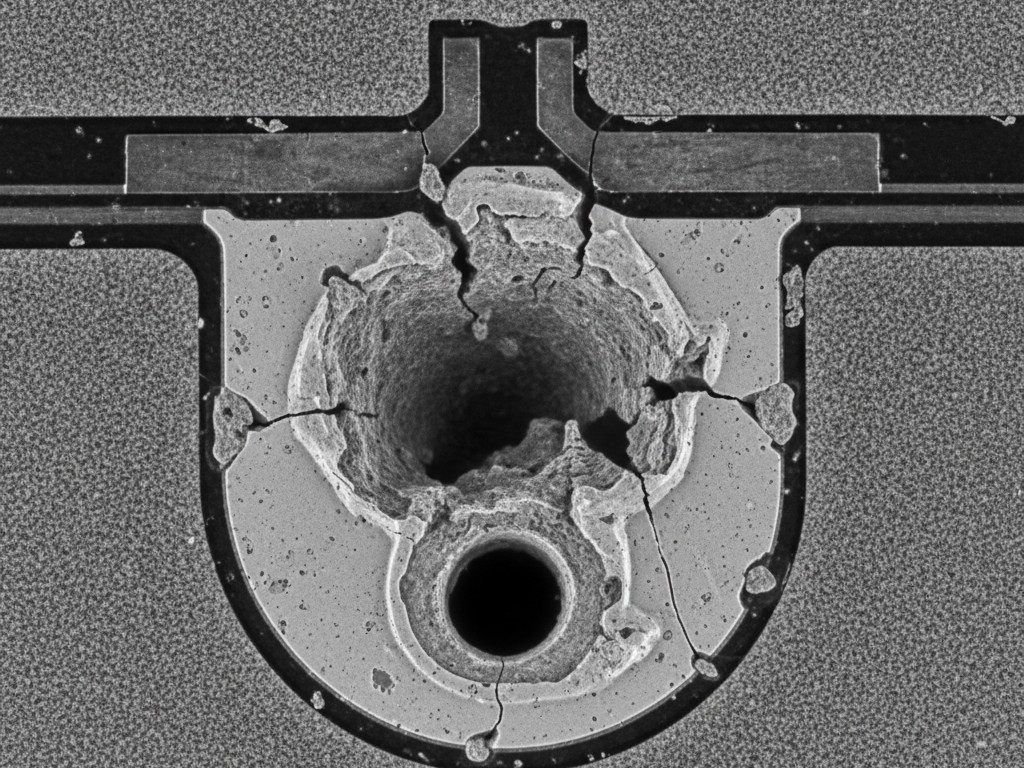 A microscopic cross-section of a failed solder joint on a circuit board. A large, crater-like void has erupted through the center of the solder, which should be solid, demonstrating the volcano effect.