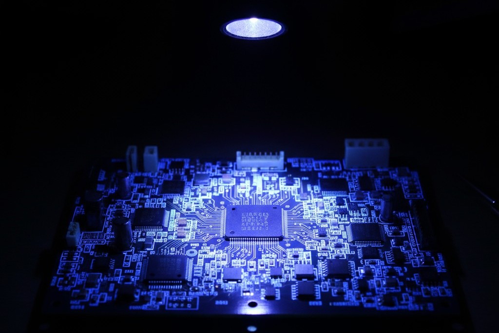 UV Light Inspection of a Conformal Coated PCB A circuit board under an ultraviolet light, causing the conformal coating to fluoresce with a bright blue glow, revealing the coverage and any defects.